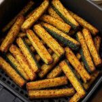 Crispy golden air fryer zucchini fries in a black basket, perfectly seasoned and ready to serve with dipping sauce.