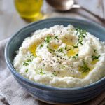 Creamy keto cauliflower mash topped with olive oil, black pepper, and fresh herbs in a ceramic bowl