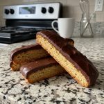 Homemade keto orange chocolate biscuits coated with sugar-free chocolate, stacked on a kitchen counter.