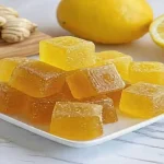 Golden keto honey lemon turmeric gummies stacked on a white plate with fresh lemon and turmeric in the background