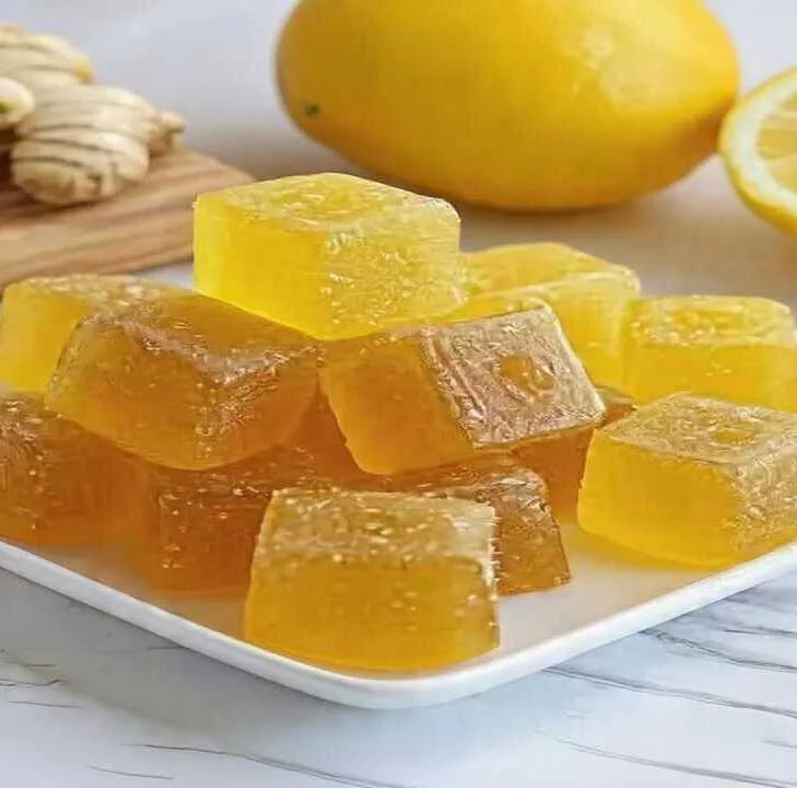 Golden keto honey lemon turmeric gummies stacked on a white plate with fresh lemon and turmeric in the background