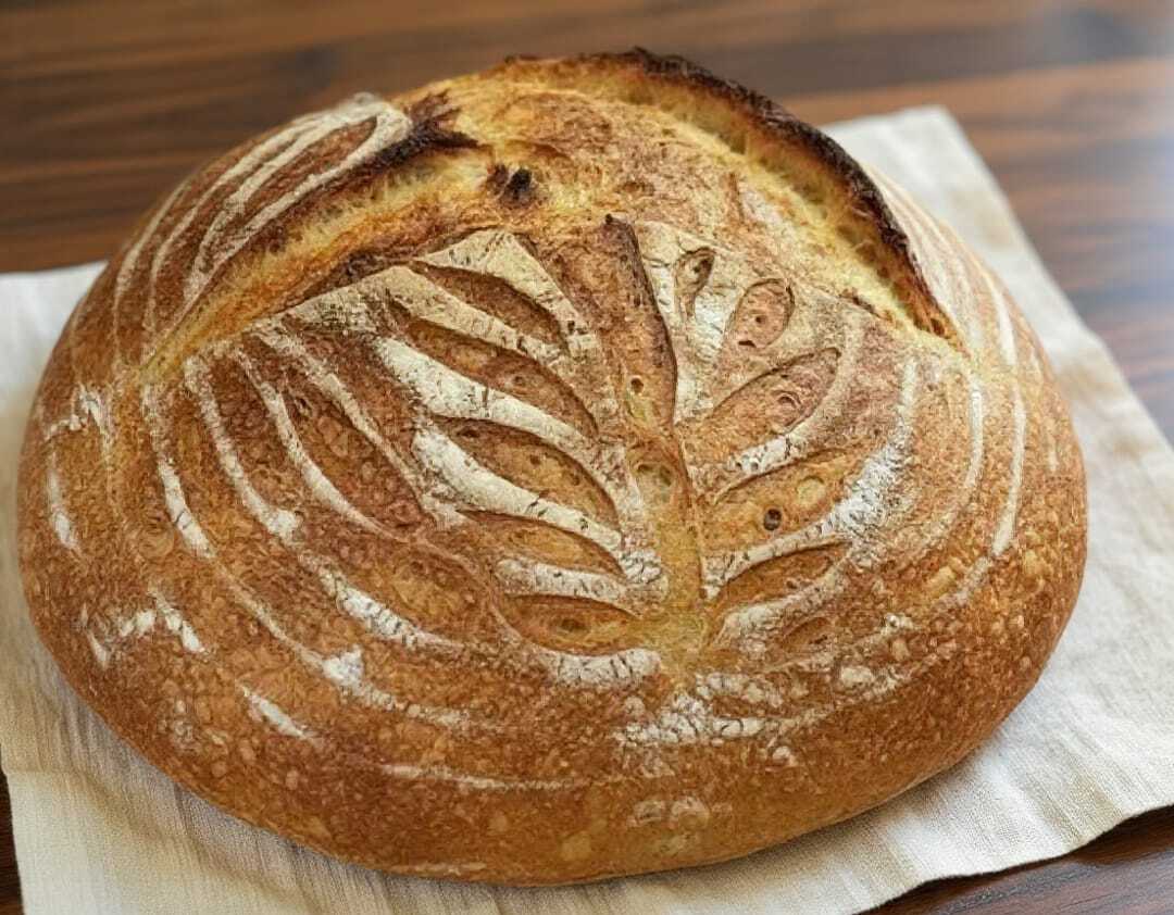 Rustic keto sourdough bread with artisan leaf scoring on a wooden surface