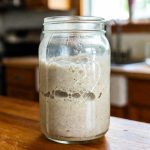 Keto sourdough starter bubbling in a glass jar with rustic background